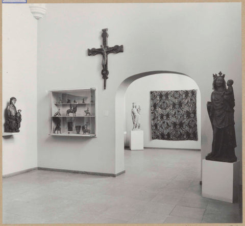 Room with medieval sculptures including Mary with child, a display case, a crucifix and a passage with a view of a tapestry and a statue of the Virgin Mary, 1961 Canvas Print