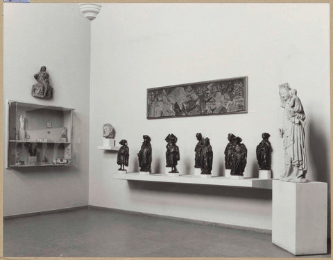 Room with medieval sculptures including Mary with child, funerary figures, a tapestry (?) and a display case, 1962 Canvas Print